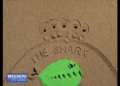 The Shark title drawn in sand beside a green shark cutout